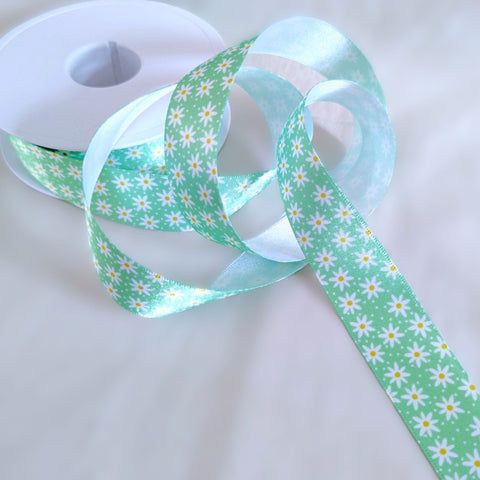 Close-up of a green satin ribbon printed with white daisies and yellow centres, 15mm wide