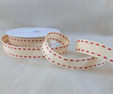 Close‑up of cream grosgrain ribbon showing red satin saddle‑stitch edging and textured weave.