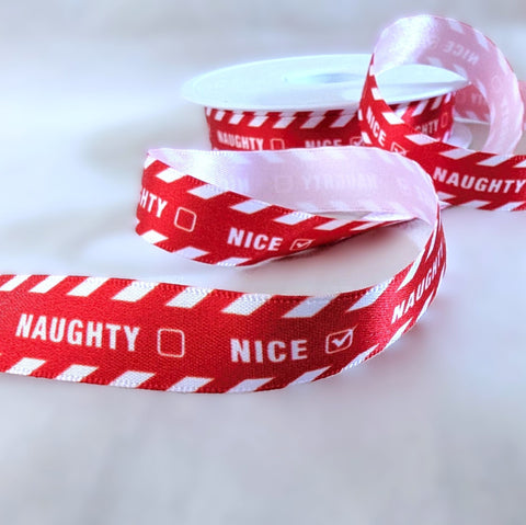 Red and white 16mm Naughty or Nice printed Christmas satin ribbon on a spool.