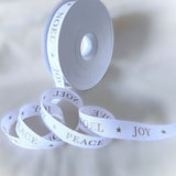 White Christmas ribbon unwound from a reel, displaying metallic Noel, Joy and Peace print. ⠋