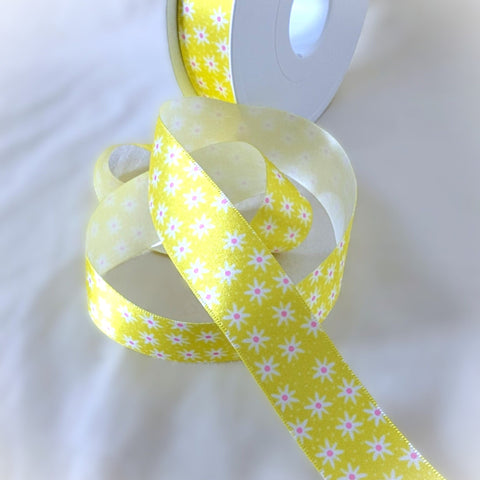 15mm Yellow floral satin ribbon with a daisy flower print unrolled beside its spool, perfect for crafts and party decorations