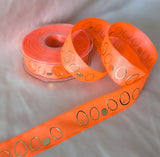 Angled view of 25mm fluoro orange wired taffeta ribbon on the reel, highlighting the wire edge and gold‑embossed pattern.