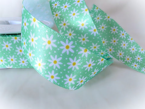Close-up of a green satin ribbon printed with white daisies and yellow centres, 25mm wide