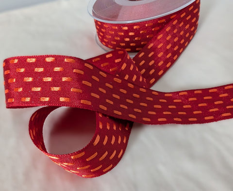 Red taffeta ribbon with orange parallel stitch detail, shown partially unrolled from the spool on a white background