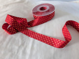 Red and orange parallel‑stitch craft ribbon unspooled from its reel and arranged in soft curves on a clean white surface