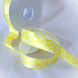 Yellow floral satin ribbon with a daisy flower print unrolled beside its spool, perfect for crafts and party decorations