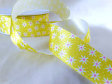 Close-up of a yellow satin ribbon printed with white daisies and pink centres, 25mm wide